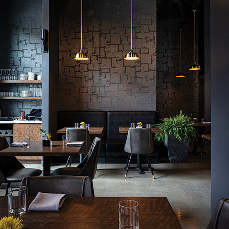 Warm brass lighting, dramatic walls, and black-upholstered banquettes exude a sophisticated vibe at Urban Restaurant