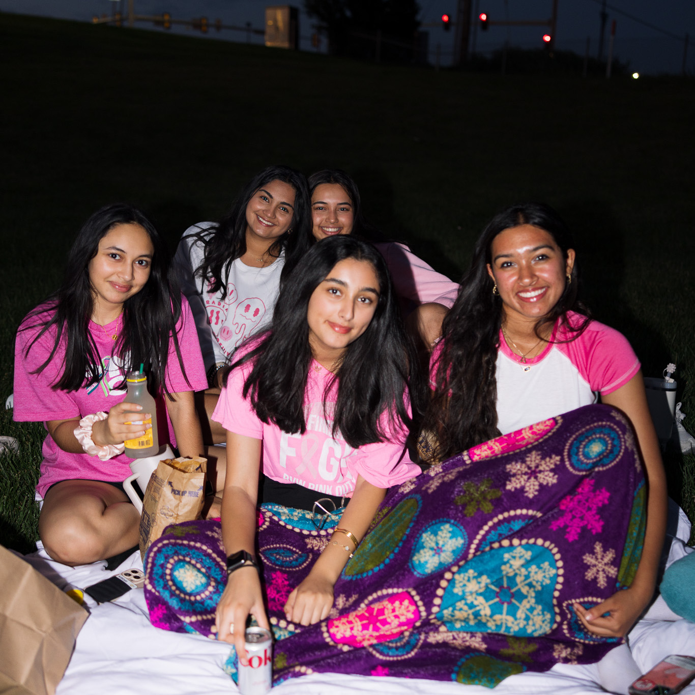 A group of women sit on a blanket at Bluhawk at night