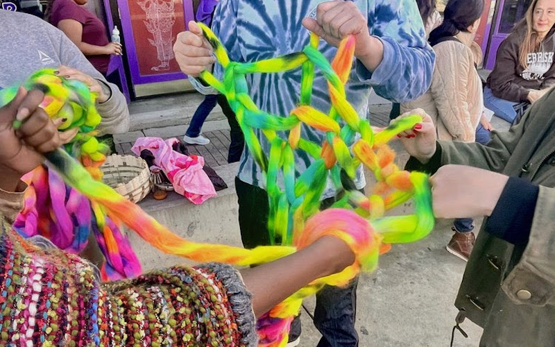 Three people arm knitting with colorful yarn